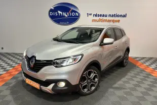 Renault Kadjar gris en 3/4 avant droit, phares et antibrouillards allumés, jantes alliage distinctives visibles.