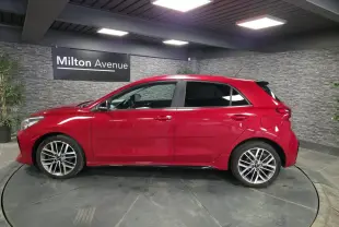 Profil droit d'une KIA RIO rouge métallisée 2022 avec jantes alliage 17'' et vitres surteintées en intérieur showroom.