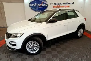 Vue 3/4 avant droite du Volkswagen T-ROC blanc avec jantes alliage et barres de toit noires en intérieur showroom.