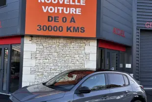 Peugeot 208 Hybrid 136 eDCS6 GT gris foncé vue 3/4 avant, avec jantes alliage et feux LED distinctifs.