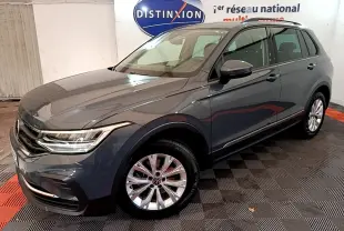 Volkswagen Tiguan gris clair en 3/4 avant droit, avec jantes alliage et feux LED allumés.
