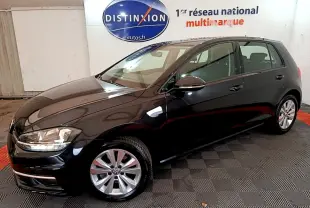 Volkswagen Golf noire vue en 3/4 avant droit, avec jantes alliage et phares allumés en intérieur showroom.