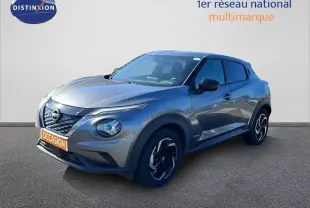 Nissan Juke Hybrid gris squale métal en 3/4 avant droit, avec calandre noire et phares ronds distinctifs.