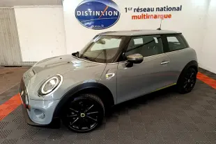 Vue 3/4 avant droit d'une MINI Cooper SE Greenwich gris foncé avec jantes noires dans un showroom.