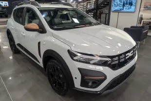 Vue 3/4 avant gauche d'une Dacia Sandero Stepway TCe 110 blanche avec rétroviseurs bronze et jantes noires en showroom.