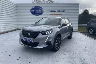 Peugeot 2008 gris Artense en 3/4 avant droit, avec calandre noire et feux LED distinctifs, stationnée devant un mur blanc.
