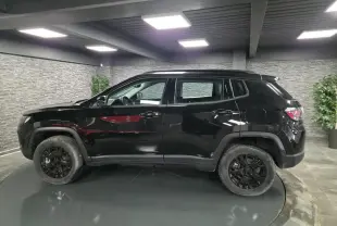 Profil côté gauche du Jeep Compass noir 2024 avec jantes noires et garde au sol surélevée en intérieur showroom.