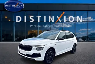 Vue 3/4 avant d'un Skoda Kamiq blanc nacré avec jantes noires et toit panoramique devant une vitrine Distinxion.
