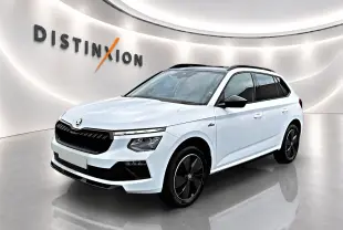 Vue 3/4 avant d'un Skoda Kamiq blanc nacré avec jantes noires et toit panoramique en showroom lumineux.