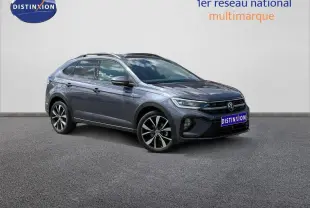 Volkswagen Taigo gris Ascot en 3/4 avant droit avec jantes alliage et barres de toit visibles.