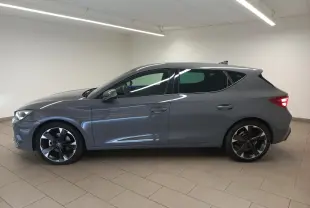 Vue de profil droit d'une CUPRA Leon Phase 2 gris Graphene avec jantes noires bicolores dans un intérieur neutre.