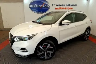 Nissan Qashqai blanc en 3/4 avant droit, avec jantes alliage noires et toit vitré visible en intérieur showroom.