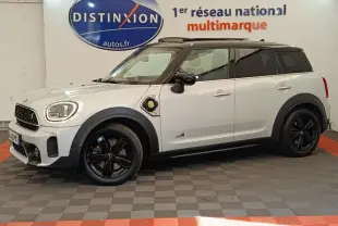 Vue latérale droite d'une MINI Countryman Cooper SE hybride blanche avec toit noir et jantes noires en intérieur showroom