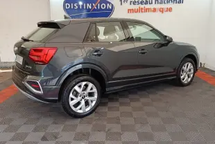 Audi Q2 gris foncé vue de profil côté droit, avec jantes alliage et feux arrière LED visibles en intérieur showroom.