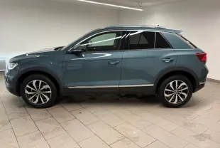 Vue de profil côté gauche d'un Volkswagen T-Roc 2025 bleu pétrole avec jantes alliage et toit ouvrant.