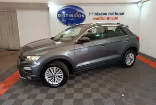 Volkswagen T-Roc gris foncé vu de profil côté gauche dans un showroom avec logo Distinxion en arrière-plan.