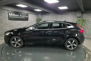 Profil côté gauche d'une Volvo V40 D2 R-Design noire métallisée avec jantes alliage Ixion 17 pouces dans un showroom.