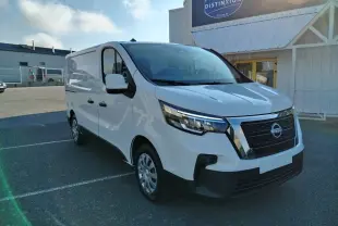 Nissan Primastar blanc en 3/4 avant droit, utilitaire avec calandre noire et détails chromés sous un ciel bleu.