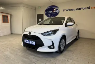 Vue 3/4 avant droite d'une Mazda2 blanche 2023 hybride, avec calandre noire et plaque "OCCASION" en intérieur showroom.
