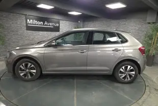 Profil côté gauche d'une Volkswagen Polo gris métallisé 2020 avec jantes alliage et vitres teintées en intérieur showroom.