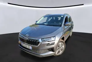 Vue 3/4 avant droite d'un Skoda Karoq gris 2023 avec jantes alu 17'' et calandre chromée, en intérieur showroom.