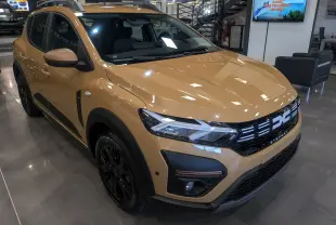 Vue 3/4 avant droite d'une Dacia Sandero Stepway beige Safari avec jantes noires et détails noirs contrastants.