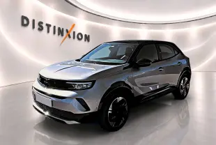 Opel Mokka Electric gris en 3/4 avant droit, avec toit noir et jantes alu distinctives dans un showroom lumineux.