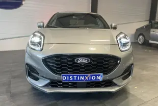 Vue frontale d'un Ford Puma gris clair avec calandre noire hexagonale et phares LED allumés en intérieur showroom.