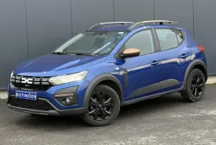 Vue 3/4 avant droite de la Dacia Sandero Stepway Bleu Iron avec jantes noires et barres de toit gris Mégalithe.