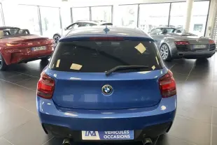 Vue arrière d'une BMW Série 1 135 i 320CV bleu métal 2013 dans un showroom avec échappements doubles visibles.