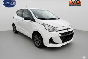 Hyundai i10 blanc vue 3/4 avant droit avec jantes alliage et feux diurnes allumés sur fond neutre.