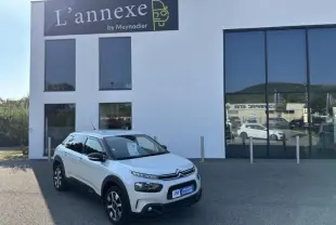 Citroën C4 Cactus blanc en 3/4 avant droit devant un bâtiment moderne avec grandes fenêtres réfléchissantes.