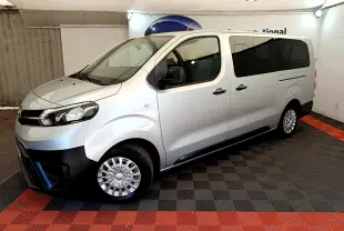 Vue côté gauche en 3/4 avant d'un Toyota Proace Verso gris clair avec vitres arrière teintées et jantes acier.