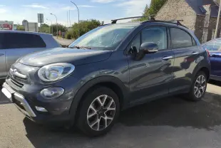 Vue 3/4 avant droite d'un FIAT 500X gris 2017 avec barres de toit et jantes distinctives en alliage.