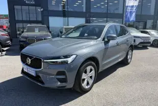 Volvo XC60 gris tonnerre vu en 3/4 avant droit, stationné devant un showroom avec calandre marquée et jantes argentées.