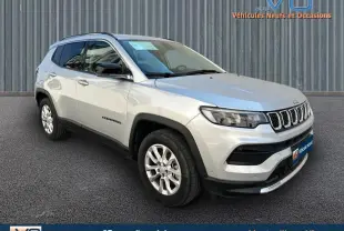 Jeep Compass gris clair en 3/4 avant droit avec barres de toit et jantes alliage 17 pouces visibles.