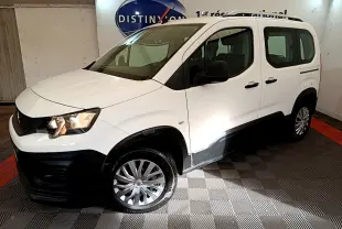 Vue 3/4 avant gauche d’un Peugeot Rifter blanc avec protections noires et jantes alliage, en intérieur showroom.