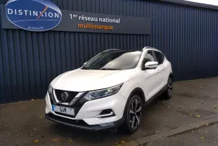 Nissan Qashqai blanc vue 3/4 avant droit, avec jantes alliage noires et calandre chromée, stationné devant un mur bleu.