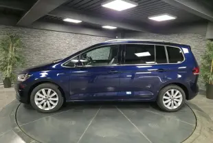 Profil côté gauche d'un Volkswagen Touran bleu métallisé 2024 dans un showroom avec jantes alliage 17 pouces.