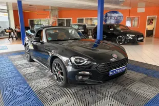 Fiat 124 Spider noir vue 3/4 avant droit en intérieur, capote ouverte et jantes foncées distinctives.