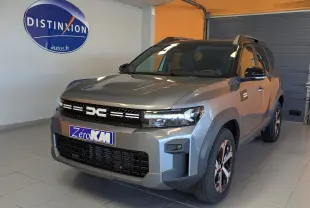 Vue 3/4 avant d'un Dacia Bigster Hybrid 155 gris schiste avec jantes alliage et toit bi-ton noir en intérieur showroom.