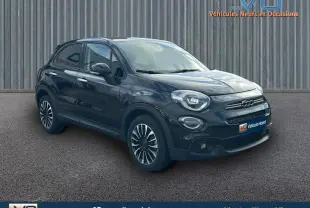 Vue 3/4 avant d'une FIAT 500X noire avec jantes classiques 16 pouces sur un sol goudronné devant un mur métallique.