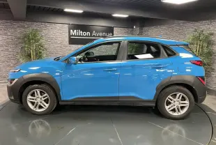 Vue de profil côté gauche d'un Hyundai Kona 1.6 CRDi Hybrid 48V bleu avec protections noires et jantes alliage 16 pouces.