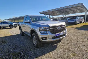 Ford Ranger Super Cabine gris Iconic vu en 3/4 avant droit sur un parking extérieur sous un ciel bleu.