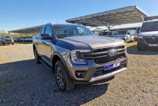 Vue 3/4 avant droit d'un Ford Ranger Super Cabine gris carbone avec calandre noire et plaques "Zero KM" sur un parking extérieur.