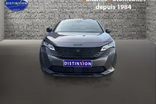 Vue avant d'un Peugeot 3008 gris foncé avec calandre noire et logo lion Dark Chrome sur fond urbain en briques.