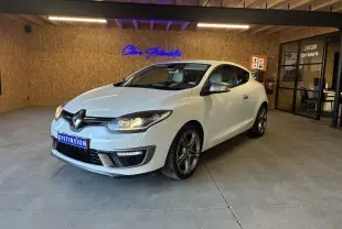 Renault Mégane Coupé blanc vue 3/4 avant droit en intérieur avec phares allumés et jantes alliage.