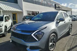 KIA Sportage gris perle en 3/4 avant droit, avec calandre noire distinctive et jantes bicolores.