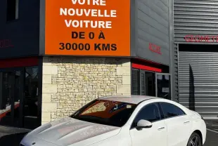 Mercedes CLA 250 e AMG Line blanc vue 3/4 avant droit, stationnée devant un bâtiment avec panneau orange Distinxion.