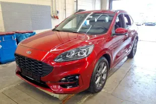 Ford Kuga 2024 rouge Lucifer en 3/4 avant droit, avec calandre noire et jantes alliage visibles en intérieur d'atelier.